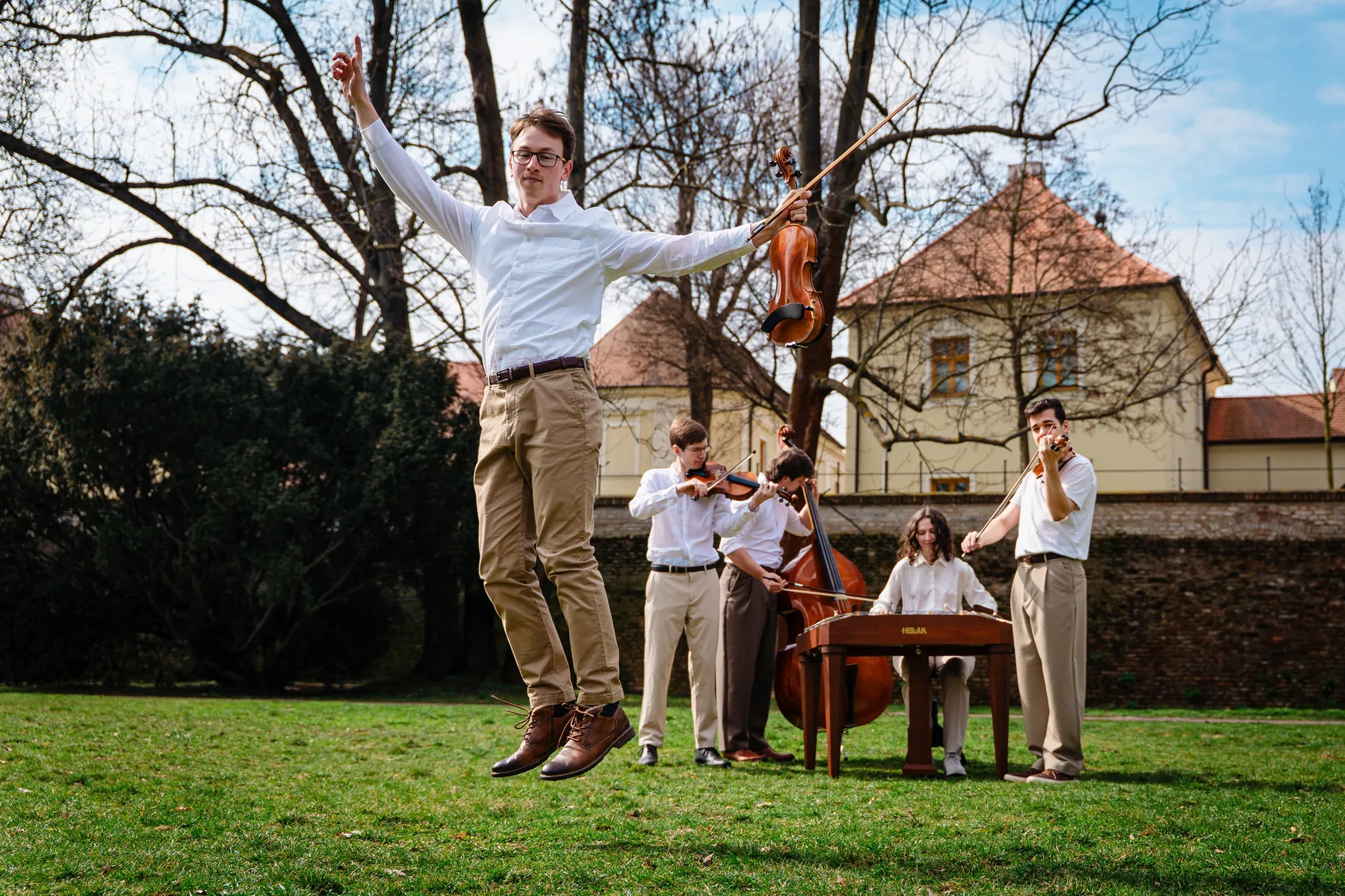 Členové kapely Zornička ve výskoku na louce při jarním focení — radostný okamžik se nástroji
